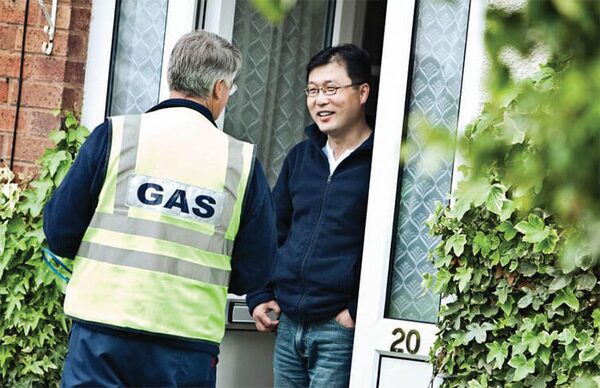 A gas engineer in a high-visibility GAS vest talking to a householder at the front door of a house