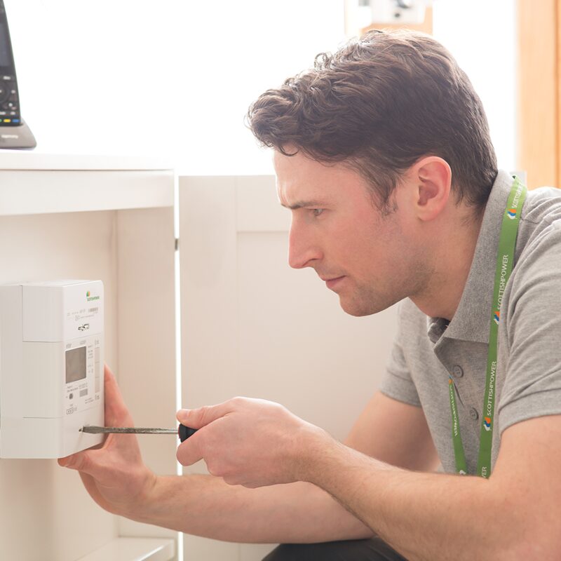 A ScottishPower engineer using a screwdriver to install a smart electricity meter in a home cupboard