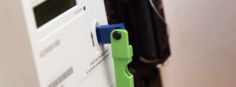 A close-up of a prepayment electricity meter with a blue key inserted and a green key holder attached