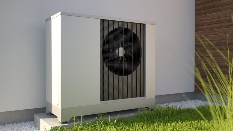 An air source heat pump unit installed outside a house wall on a concrete base with grass in the foreground