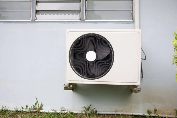 An air source heat pump outdoor unit mounted on the exterior wall of a house below a window