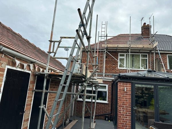 Scaffolding erected around the back of a brick semi-detached house with a conservatory, ready for solar panel installation