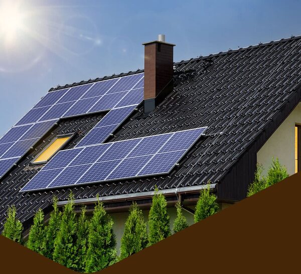 Solar panels mounted on the tiled roof of a house with a chimney and trees in front