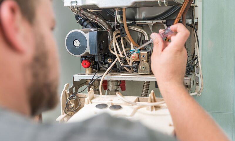 An engineer repairing the internal components of a wall-mounted gas boiler with a screwdriver