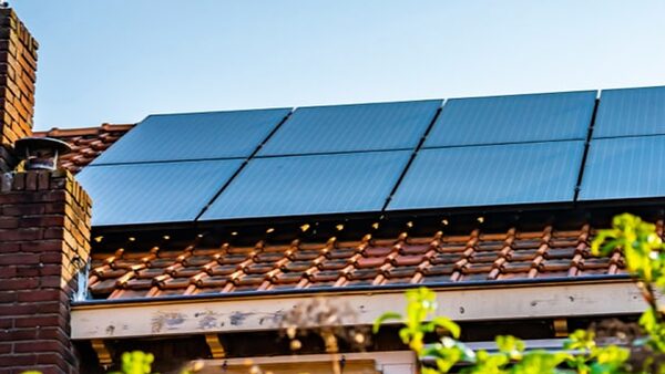 Solar panels installed on a tiled house roof next to a brick chimney on a sunny day