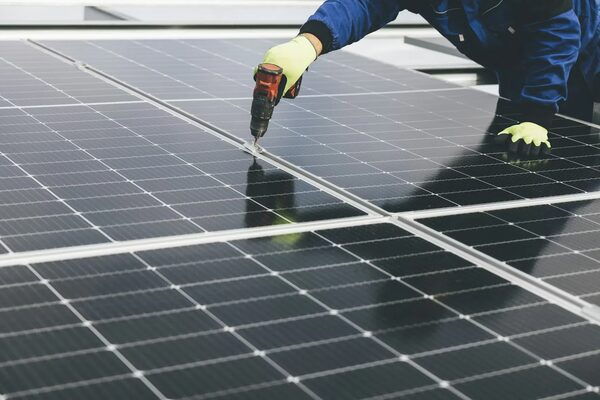An installer in gloves using a cordless drill to fix solar panels to a roof