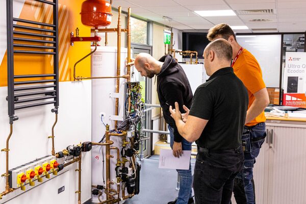 Trainees inspecting a heat pump cylinder and copper pipework rig at a Mitsubishi Electric training centre
