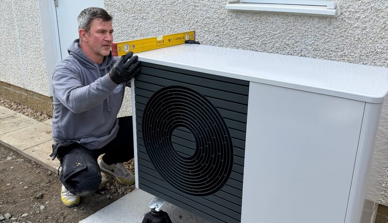 An installer using a spirit level to check an outdoor air source heat pump unit outside a house