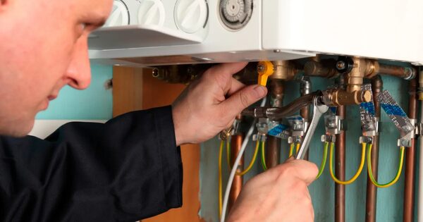 A heating engineer using a spanner to work on the pipework beneath a wall-mounted gas boiler