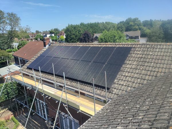 A large array of black solar panels installed on the tiled roof of a house, with scaffolding along the front of the property