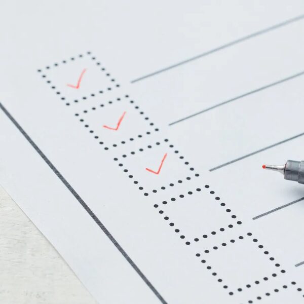 A printed checklist form with red tick marks in dotted checkboxes and a red-tipped pen resting on it