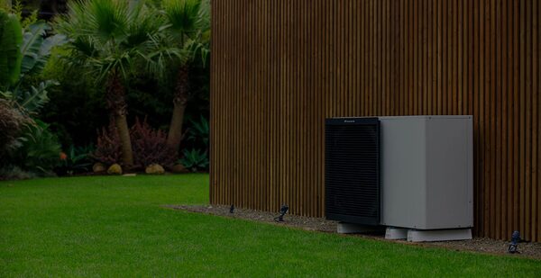A Daikin air source heat pump unit installed outside against a slatted timber garden wall beside a lawn