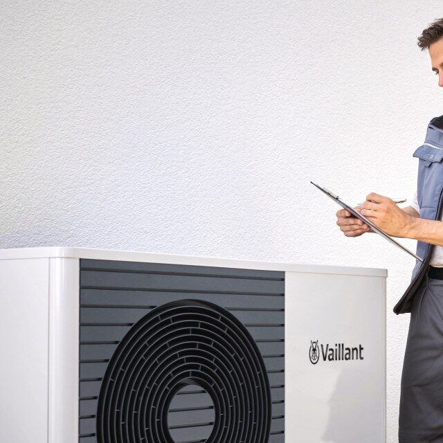 A technician with a clipboard inspecting an outdoor Vaillant air source heat pump unit