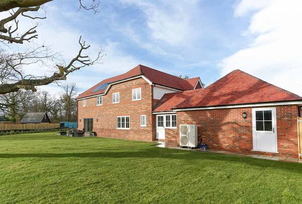 A large brick house with an air source heat pump unit installed on the exterior wall beside a garage
