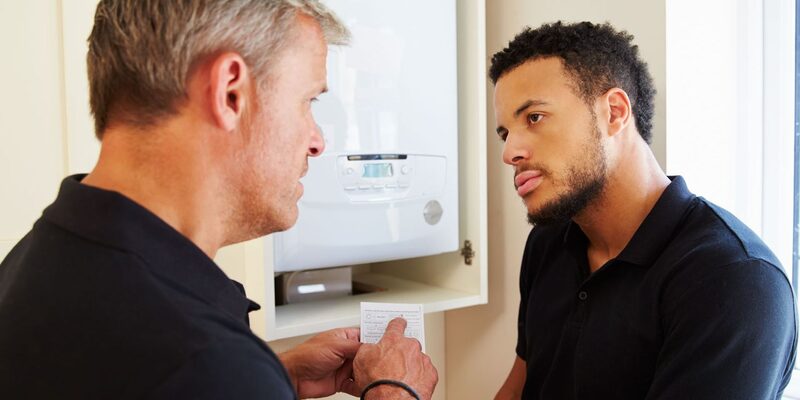 An engineer showing paperwork to a homeowner in front of a wall-mounted gas boiler