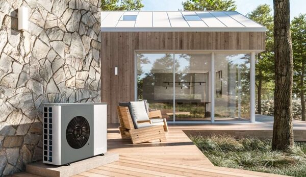An air source heat pump unit installed outside a modern timber-clad house on a wooden deck