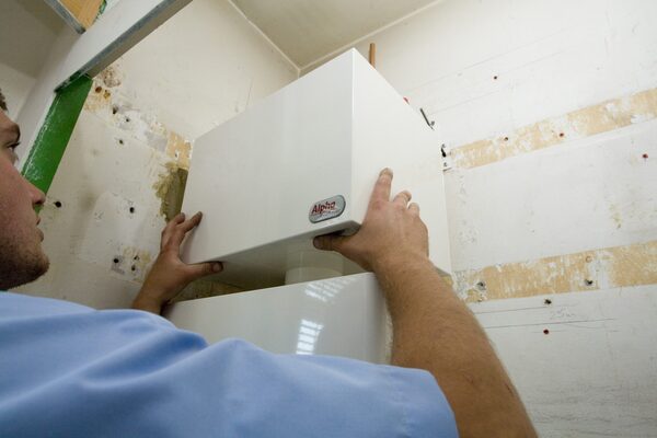 An engineer fitting a white Alpha boiler casing onto a wall-mounted boiler during installation