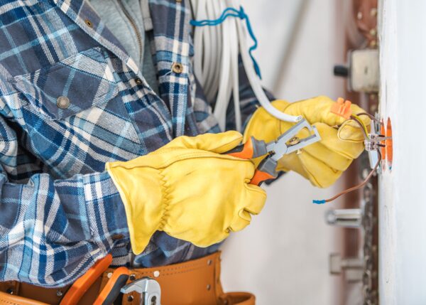 An electrician in yellow gloves using pliers to wire an electrical connection in a wall
