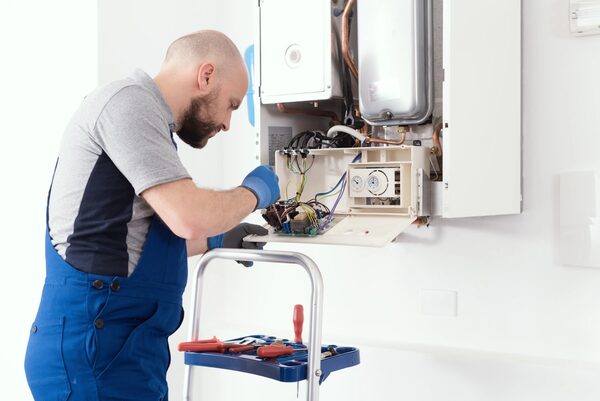 An engineer in blue overalls servicing the internal components of a wall-mounted gas boiler