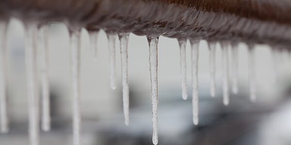 Icicles hanging from a frozen metal pipe outdoors in cold weather