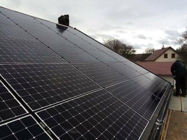 A roof covered in black solar panels with a worker installing them on a residential house