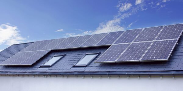 Solar panels installed on a slate-tiled house roof with two skylights under a blue sky