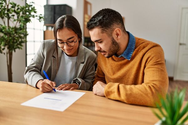 A woman signing a paper document at a table while a man watches