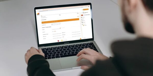 A man using a MacBook Pro laptop displaying the HETAS online notification form for solid fuel installations