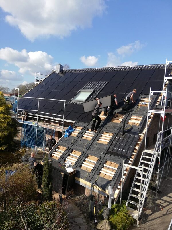 Workers on scaffolding installing solar panels on the tiled roof of a house