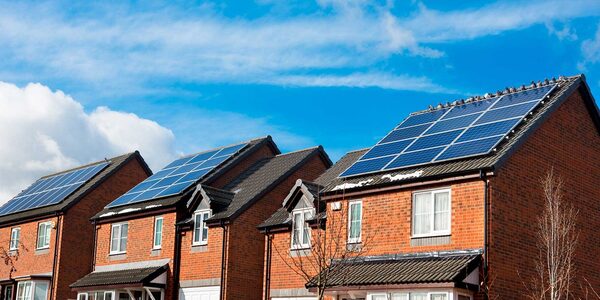 A row of brick houses with solar panels installed on their roofs under a blue sky