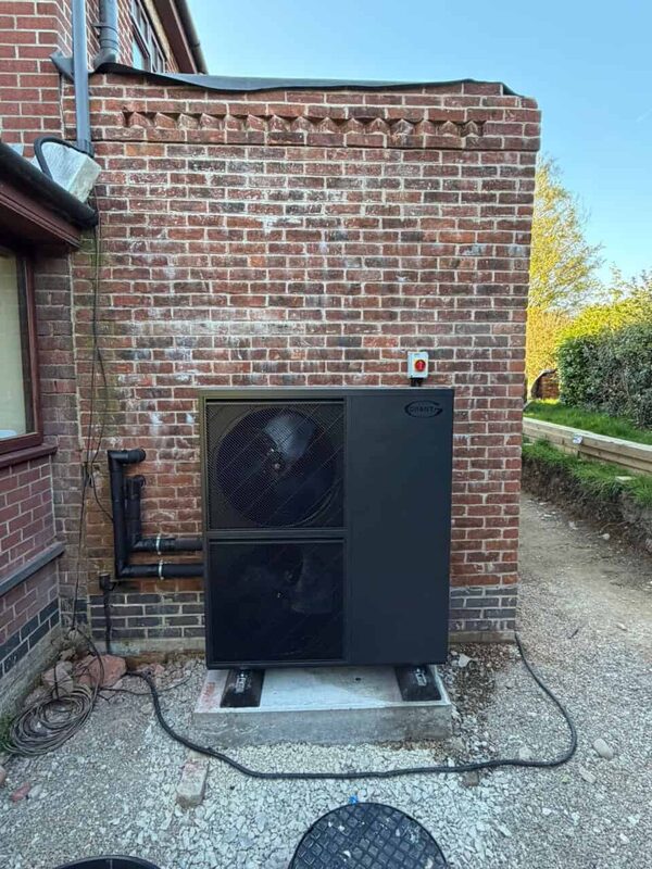 A Grant air source heat pump installed on a concrete base against a brick wall outside a house