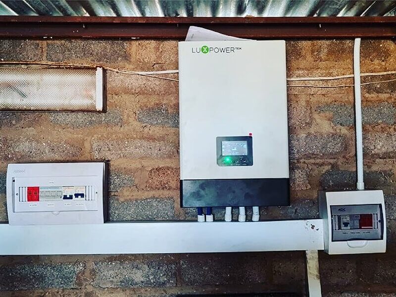 A LuxPower solar inverter mounted on a brick wall next to a consumer unit and small distribution box