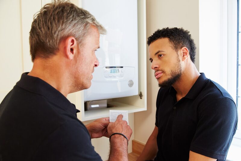 An engineer showing paperwork to a homeowner in front of a wall-mounted gas boiler