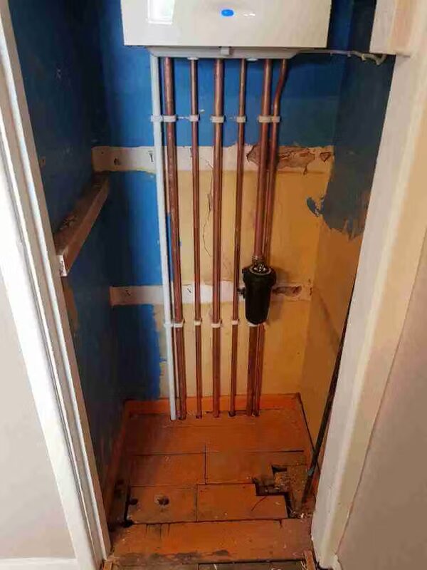 A wall-mounted boiler with exposed copper pipework in an unfinished airing cupboard during installation