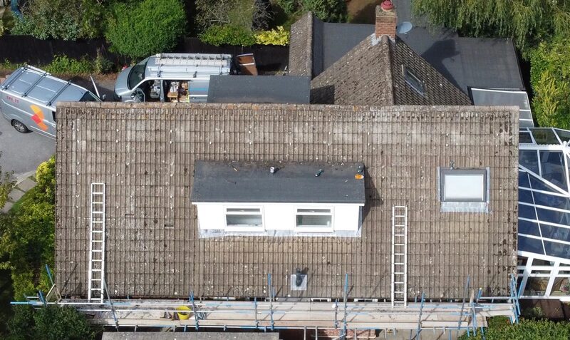 Aerial view of a tiled house roof with scaffolding and ladders before solar panel installation, with installer vans parked nearby