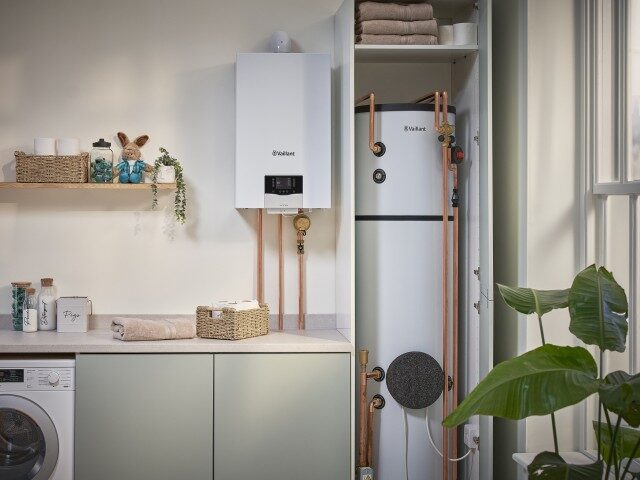 A white Vaillant wall-mounted gas boiler with copper pipework next to a hot water cylinder in an airing cupboard in a utility room