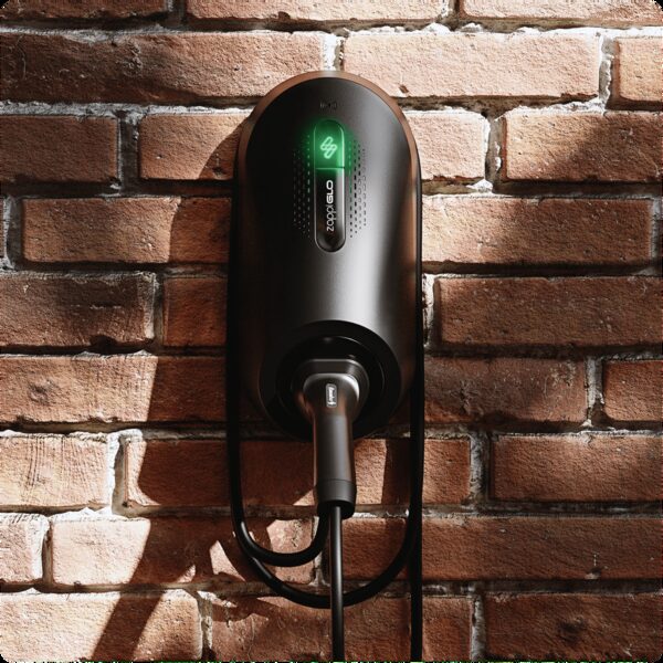 A black myenergi zappi GLO electric car charge point mounted on a brick wall with a charging cable holstered below
