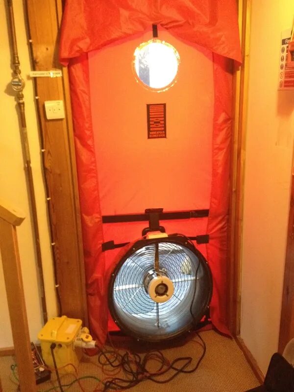 A blower door test setup with a red fabric seal and fan fitted in a doorway of a house