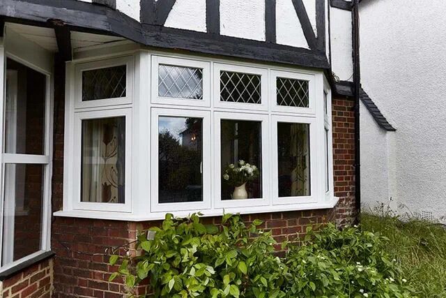 A white uPVC bay window with diamond-leaded top panes installed on a brick Tudor-style house