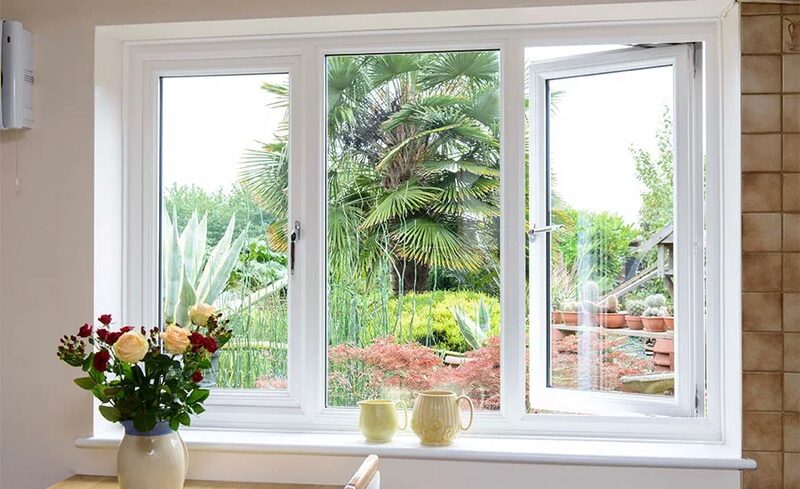 A white uPVC casement window installed in a home, with one pane open, overlooking a garden, with flowers and mugs on the windowsill