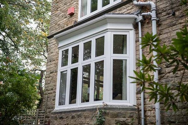 A white uPVC bay window installed on a stone-brick house exterior surrounded by trees