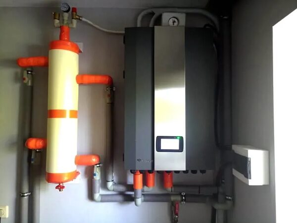 A wall-mounted heat pump or boiler unit with a buffer cylinder and insulated pipework installed in a home plant room