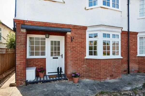 A brick house exterior with a white front door and white casement windows including a bay window