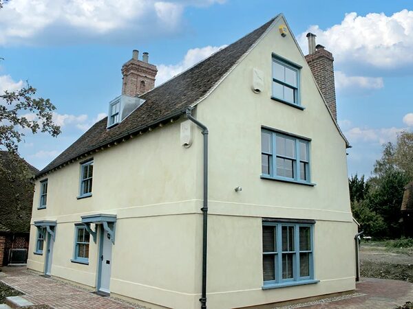 A traditional English house with cream lime-rendered walls and blue-framed sash windows, likely after lime render insulation work