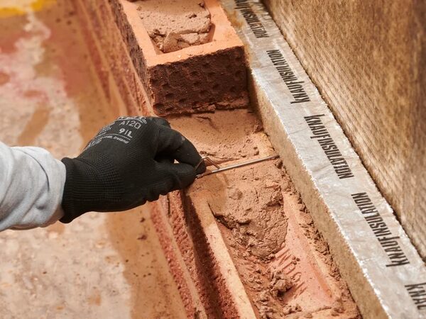A gloved worker installing a Knauf Insulation cavity barrier between brickwork and mineral wool insulation in a cavity wall