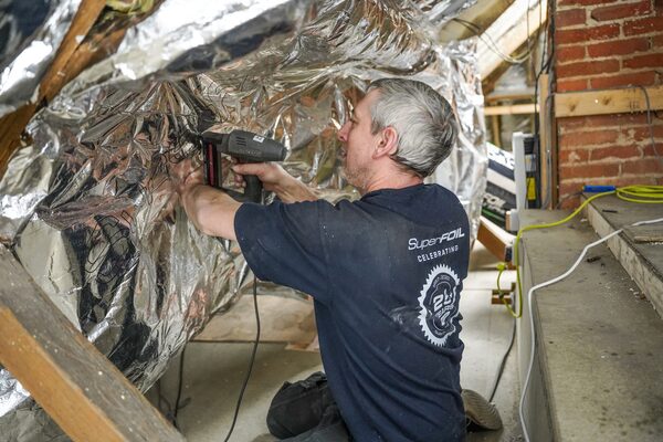 A man stapling reflective foil insulation to a sloped loft roof in an attic under renovation