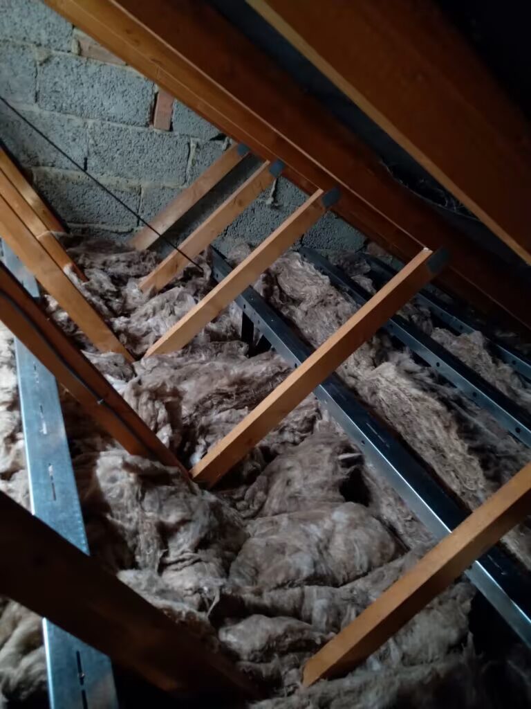 Loft space with mineral wool insulation laid between joists under wooden rafters