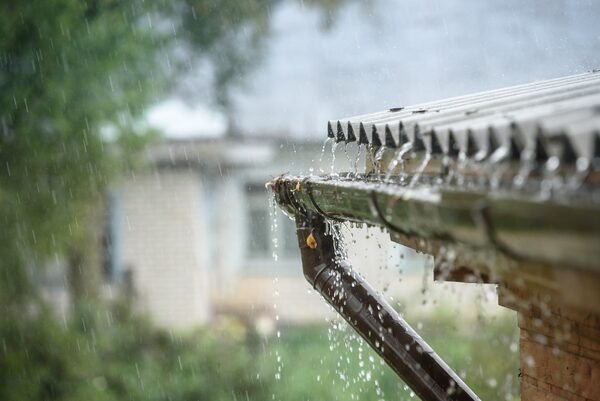 Rainwater pouring off a house roof into a blocked overflowing gutter and downpipe during heavy rain