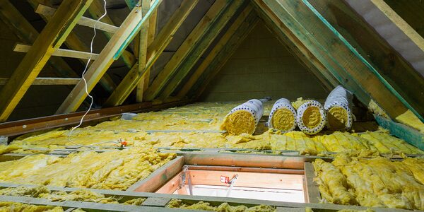 Rolls of yellow glass-fibre insulation laid between joists in a loft with an open hatch