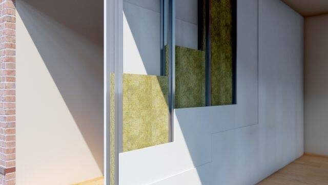 A cutaway render of a wall showing ROCKWOOL stone wool insulation slabs fitted within a stud partition next to a brick wall